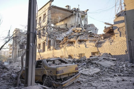 A destroyed taxi alongside a destroyed building. Rubble has been blown into the street