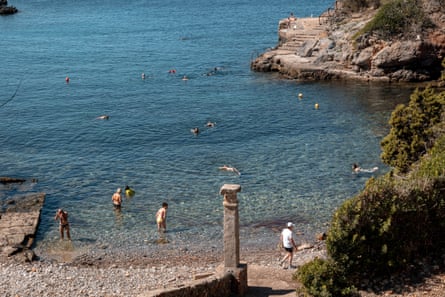 People bathe in clear sea at a stony beach