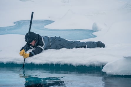 Man lies on edge of ice and lowers scientific equipment into water