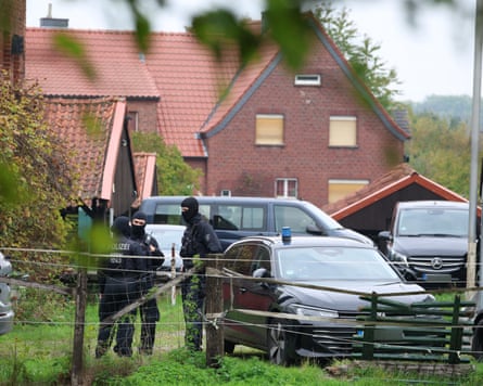 Three police officers, all wearing balaclavas, stand next to a car on what appears to be the edge of a housing estate.