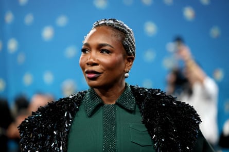 She wears a dark-green dress underneath a black sparkly coat with silver braids in her hair.