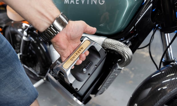 Close-up of a man removing a large Maeving-branded battery from beneath the bike’s apparent ‘petrol tank’