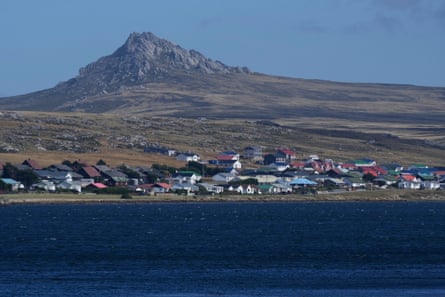 Hill against blue sky behind town with ocean in foreground