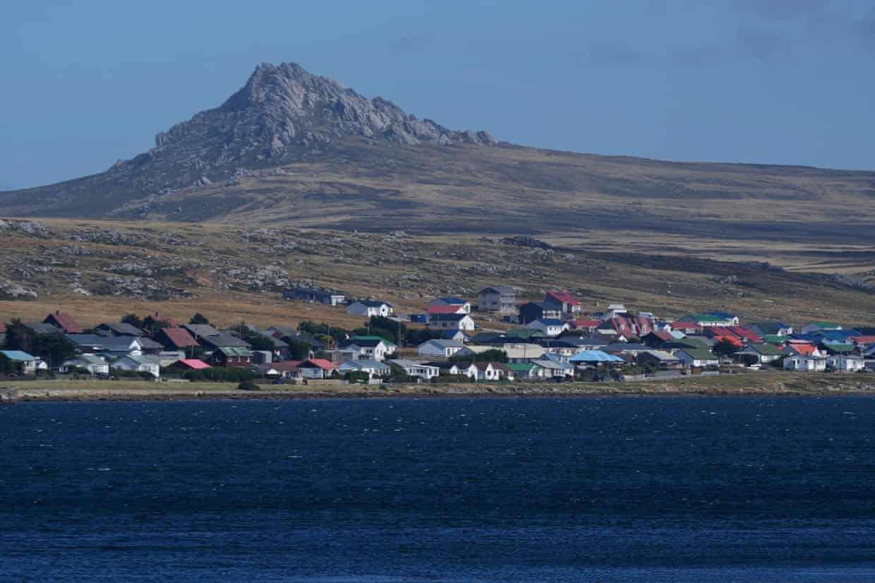 Hill against blue sky behind town with ocean in foreground