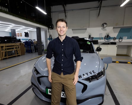 Alex Kendall stood in front of a Wayve car wearing brown chinos and a dark navy blue shirt