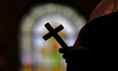 Silhouetted hand holds silhouetted cross with stained-glass window blurred in background