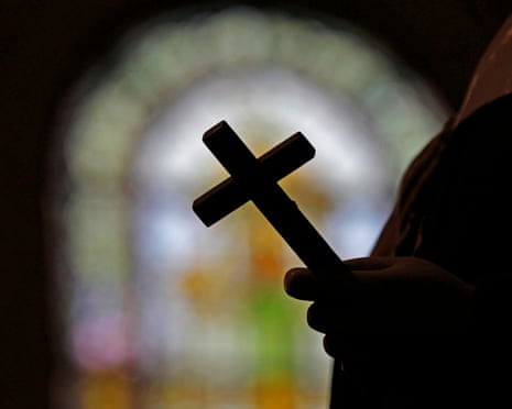Stock image of silhouetted hand holding cross, with stained glass blurry in background.