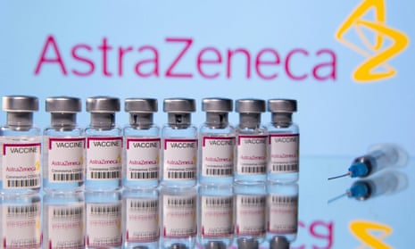 Vials labelled 'AstraZeneca Covid-19 Coronavirus Vaccine'  and a syringe are seen in front of a AstraZeneca logo