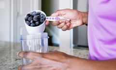 A woman makes a blueberry smoothie using a measuring cup.