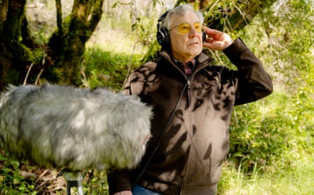 Bernie Krause wearing headphones near a sound boom by a tree