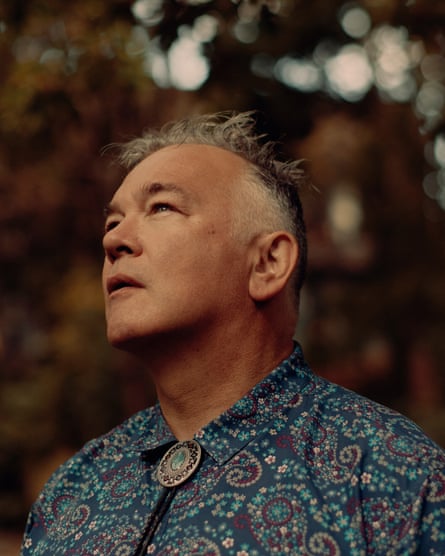 A head and shoulders photograph of Stewart Lee against a leafy background, looking up to his right