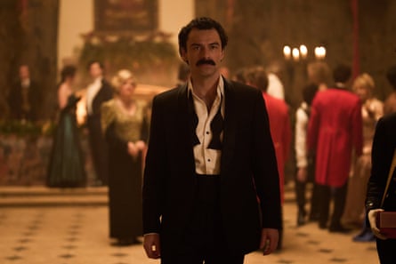 Aidan Turner stands in a grand hall during a formal event in the show