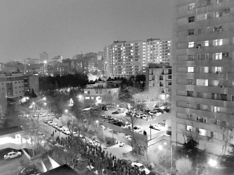 Grainy black and white image of a march in the street in Tehran at night, taken from a high vantage point in the city.