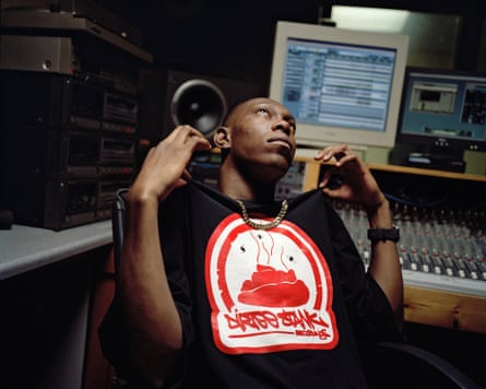 Dizzee Rascal looks up while holding the shoulders of his hoodie, in a recording studio.