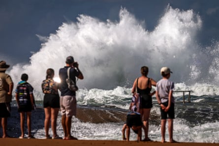 People watch a large wave breaking on a rock pool at North Narrabeen beach in Sydney