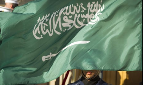 A soldier's face is covered by the Saudi flag