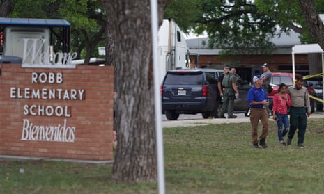 A woman walks with two men across the front lawn of an elementary school.