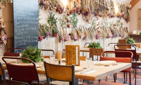 Metal-framed wooden chairs and wooden tables at the Riverford Field Kitchen, with dried bouquets hanging on the wall