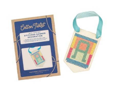 A cross-stitched wooden banner kit with a colourful letter A design and its packaging