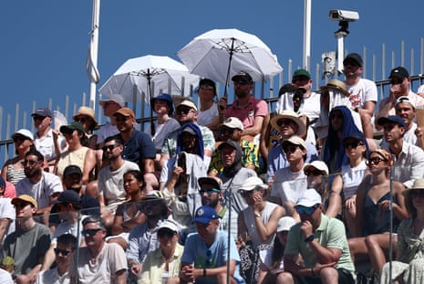 Spectators use umbrellas to take cover from the sun during the first round match between France's Moise Kouame and Croatia's Marin Cilic