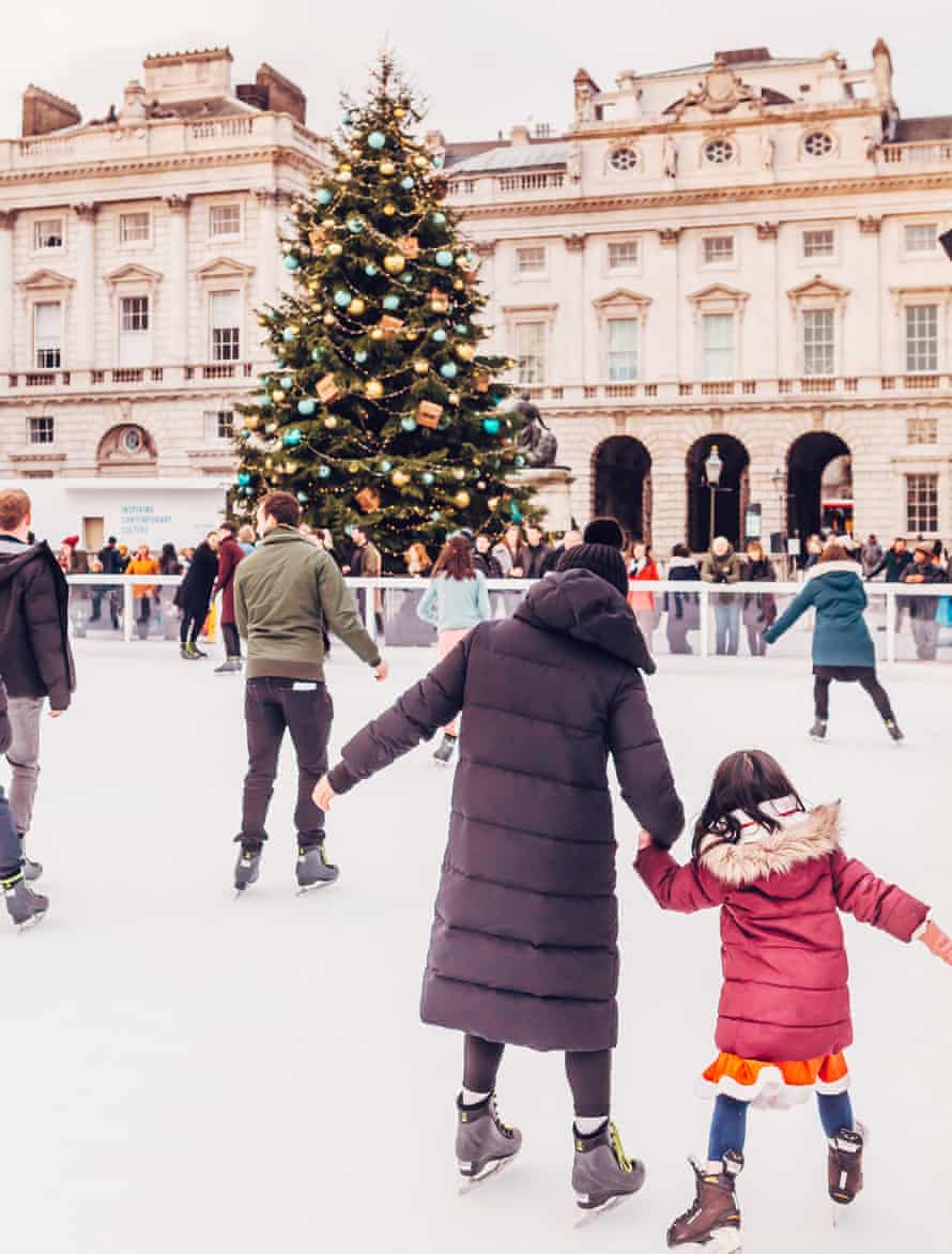 Rear view of a woman and child skating hand-in-hand on the ice rink at Somerset House in London.