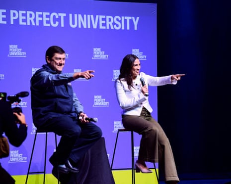 Troy Jackson and Alexandria Ocasio-Cortez, seated on stools on a stage, point at the audience