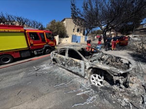 Firefighters near a burnt-out vehicle
