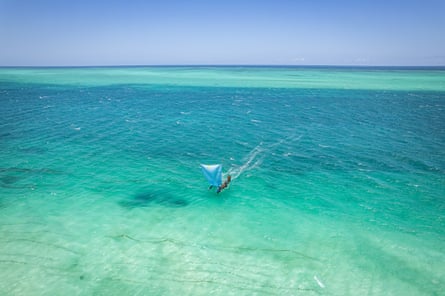 A long outrigger dugout canoe with a sail in shallow turquoise waters