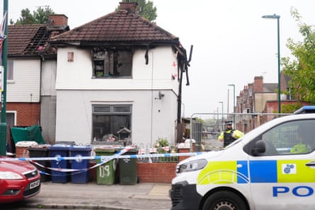 Police van, officer and police tape around house with upper storey burnt out