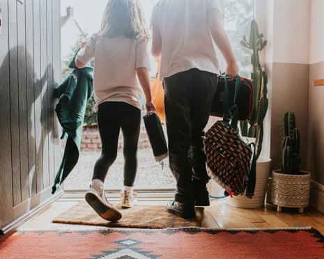 Two children carry bags and backpacks while walking out an open front door