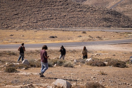 Four men walk over a bare rocky hill with a road in the background