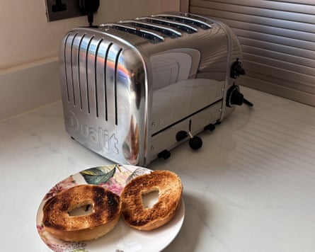 A silver Dualit 4 Slice NewGen Classic Toaster next to a plate of two bagels on a worktop