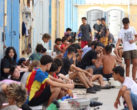 People sit on the ground and lean against a wall on a street in Ceuta