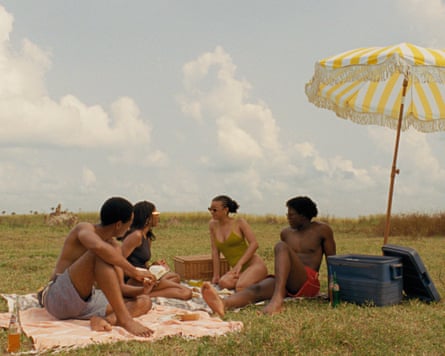 Film still showing the actors sitting under an umbrella having a picnic
