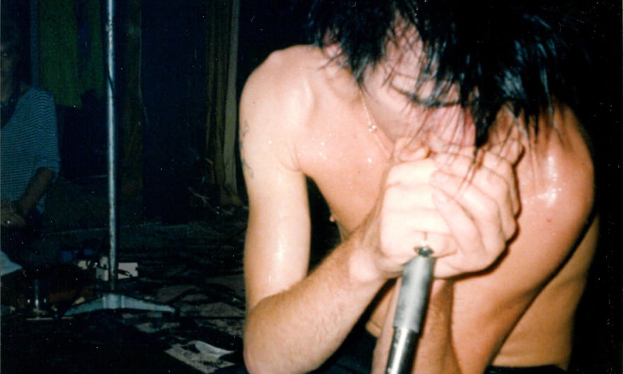 A young, shirtless Nick Cave sings into a microphone