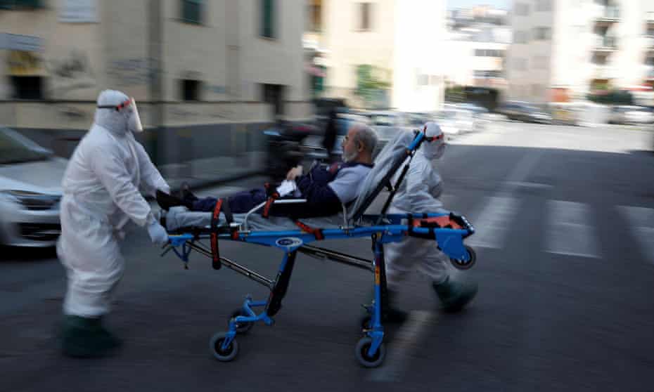 Medical staff in protective clothes carry a patient down a street in Naples.
