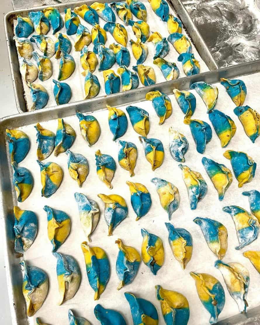 Two pans hold several dozen blue and yellow dumplings