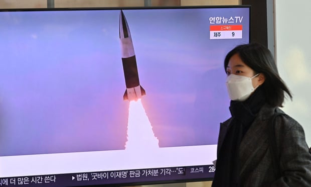 woman walks past TV screen showing footage  of a missile test