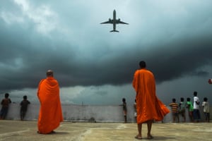 Buddhists monks and children look out from the rooftop at a Buddhist mission hostel and school for underprivileged children as an international passenger flight takes off at the Netaji Subhash Chandra Bose International Airport as the authorities eased restrictions imposed as a preventive measure against the spread of the COVID-19 coronavirus