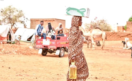 A woman carries a box of pasta on her head and a bottle of oil in her hand as aid workers drive past in a pick-up motor-tricycle