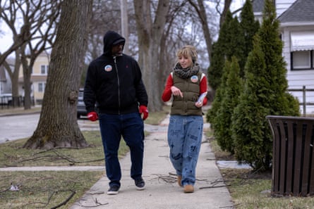 A woman speaks with a man while walking on a sidewalk.