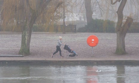 Woman pushing a pram in foggy conditions by the River Thames in Windsor.