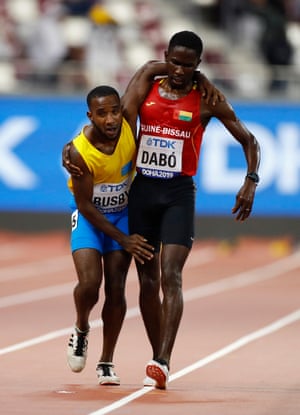 Braima Suncar Dabo, de Guinea-Bissau, ayuda a Jonathan Busby, de Aruba, a terminar en las eliminatorias de 5.000 metros masculinos durante el Campeonato Mundial de Atletismo en el Estadio Khalifa en Doha, Qatar.