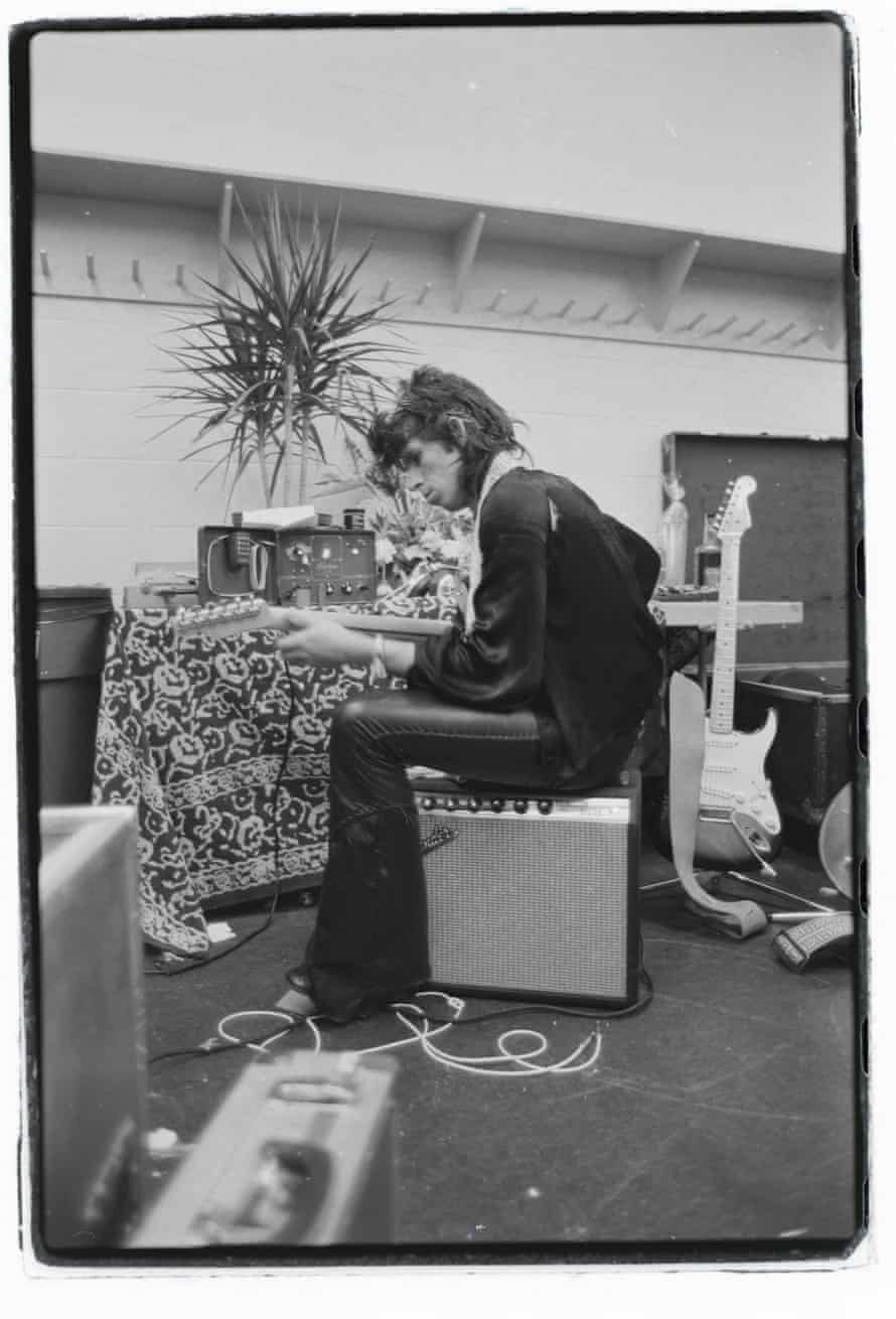 White man sitting on an amp and playing guitar