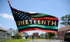A flag, in the pattern of the American flag, with green and red stripes, rainbow stars, and the word Juneteenth in yellow in the center.