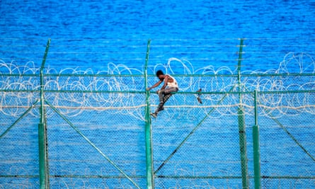 A migrant climbs a fence fortified with razor wire