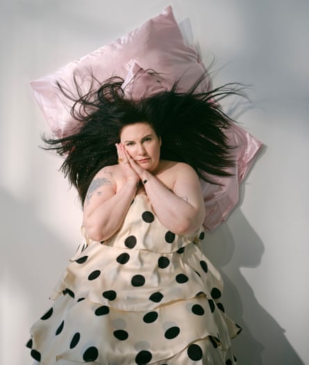 Portrait of Lena Dunham wearing a black and white polka dot dress, lying on a pink satin pillow with her dark hair fanning out over it