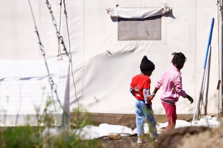 Two children stand beside a white tent.