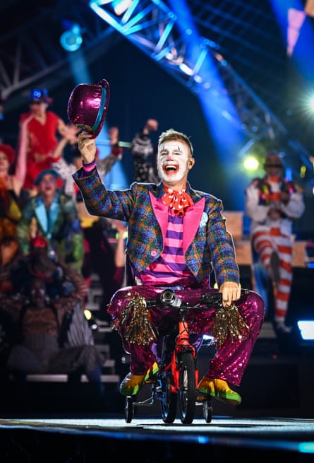Gary Barlow, dressed as a clown, rides on a kid’s bike with stabilisers