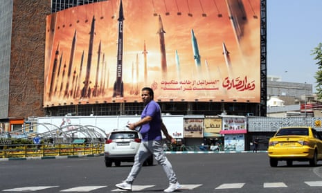 A man ⁢in Tehran walks past an anti-Israel billboard that carries the images of missiles and the words in Persian: 'Israel is weaker than spider home’